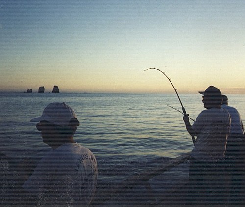 Peter holding a bent rod with Alijos Rocks in the distance at twilight
