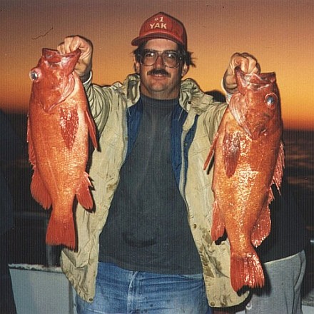 Peter holding two red rockfish at twilight